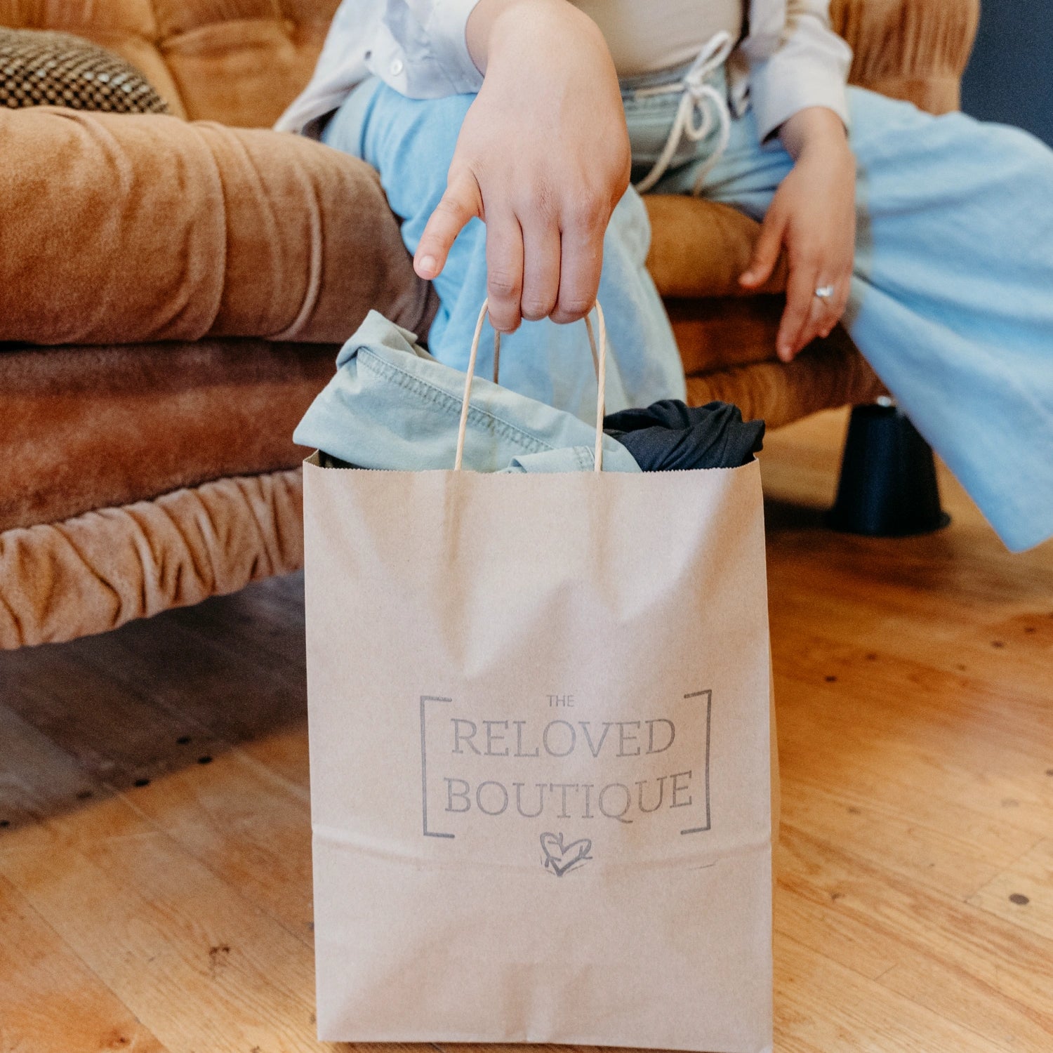 A close up shot of a paper bag filled with clothing. It has The Reloved Boutique logo stamped on it.