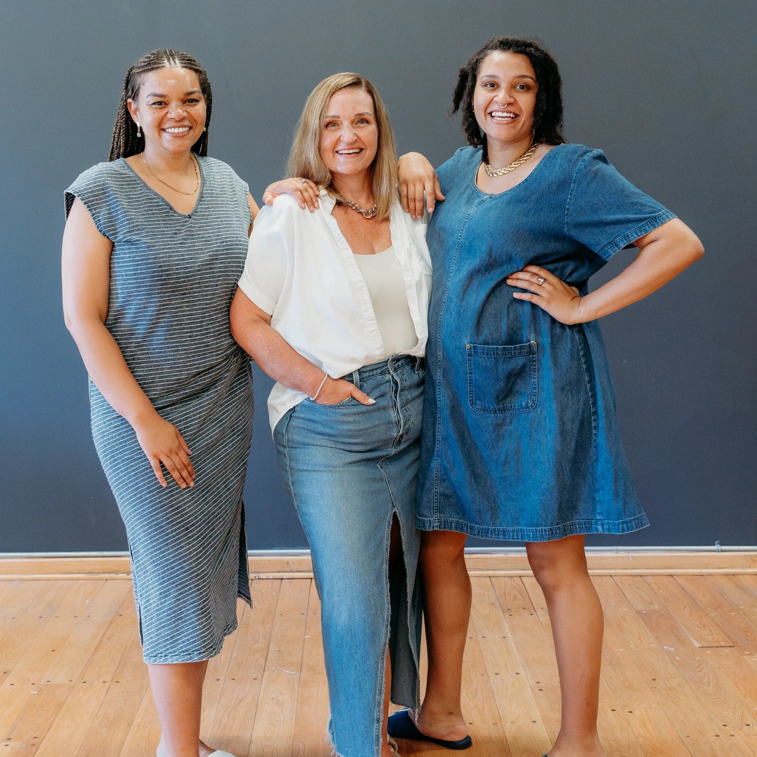 Tish, Raquel, and Lex smiling at the camera and posed in front of a blue wall.