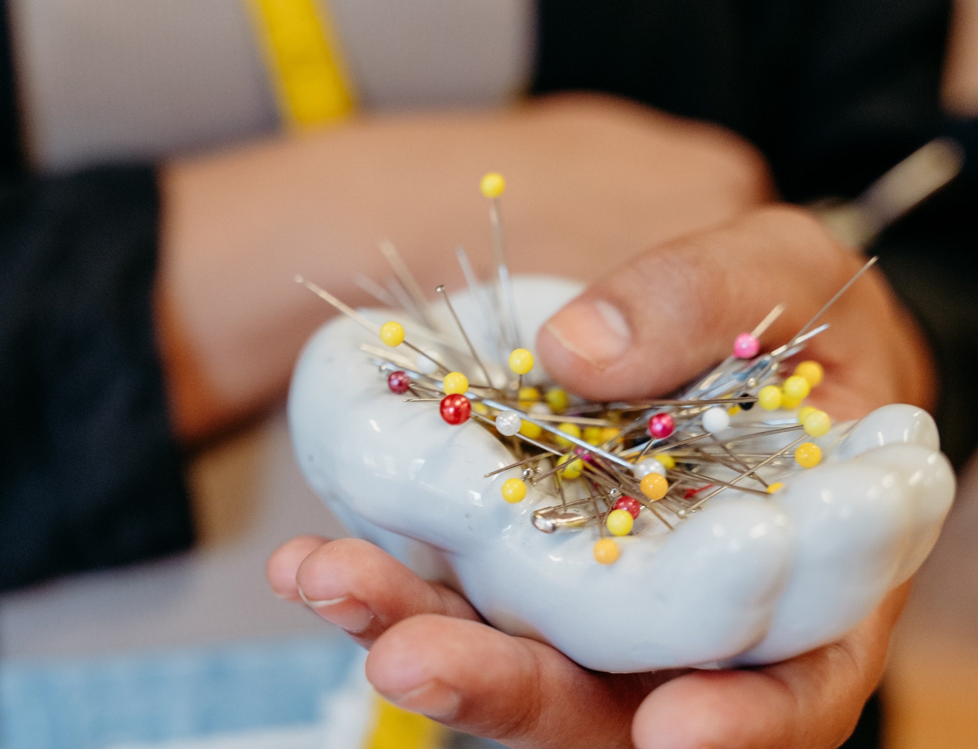 Image of a hand holding a ceramic dish filled with colorful sewing pins.